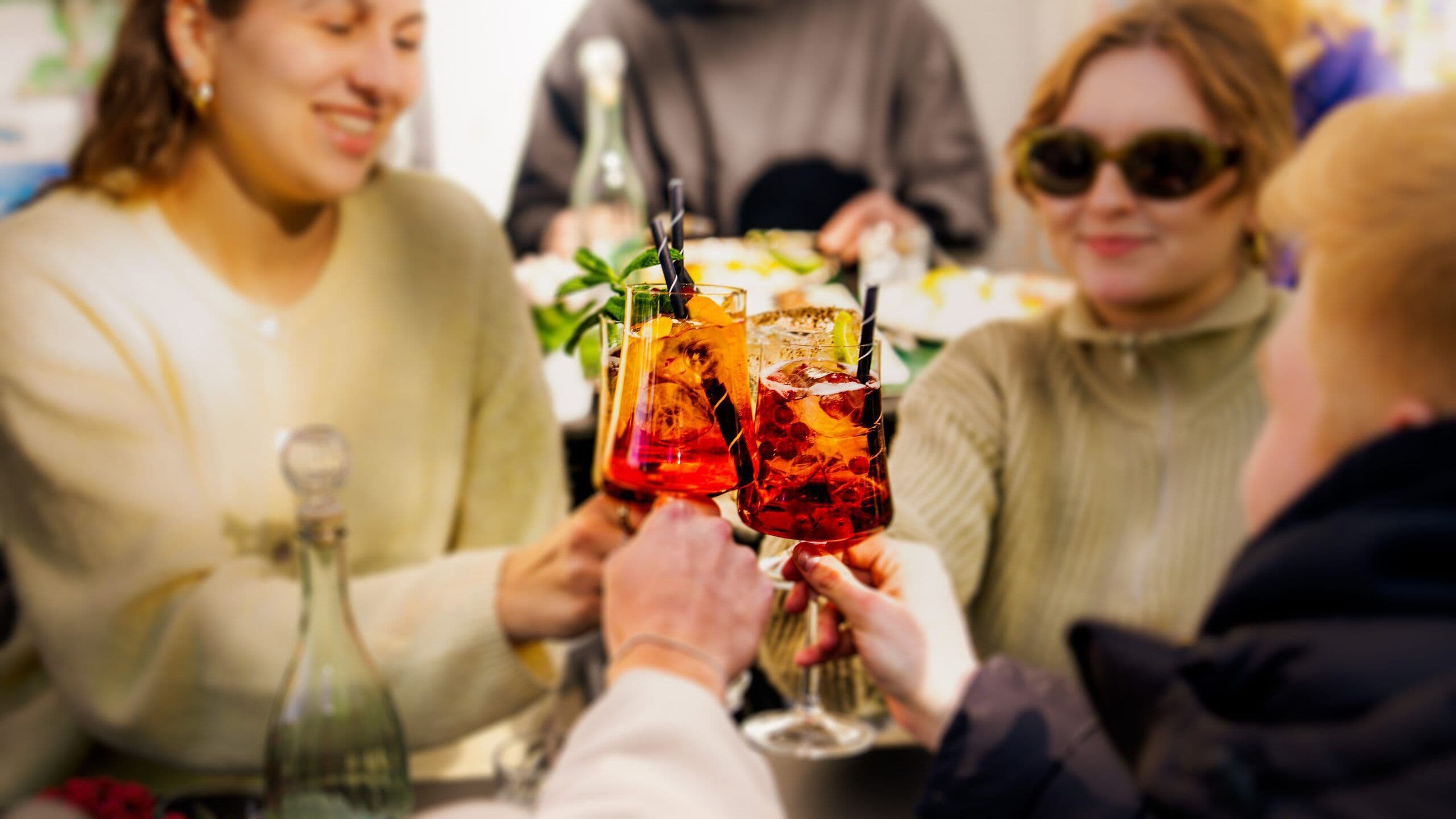 Vier Gäste stossen am Tisch mit roten Aperitif-Cocktails mit Minze und Orangenscheibe an.